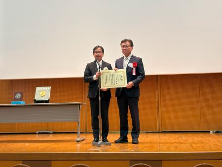 医療福祉建築賞の表彰状を持って壇上にいる様子